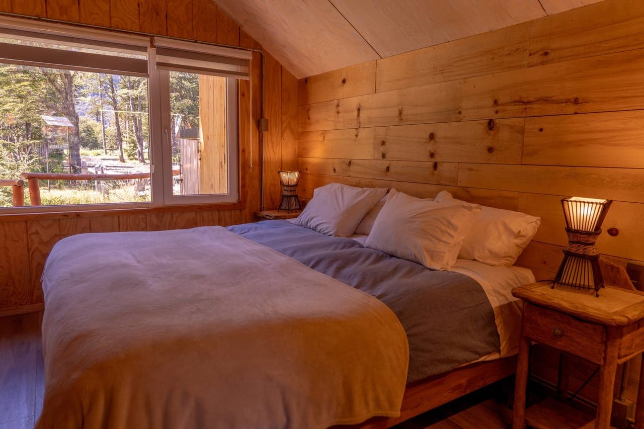 Dormitorio con cama matrimonial y ventanal al bosque
