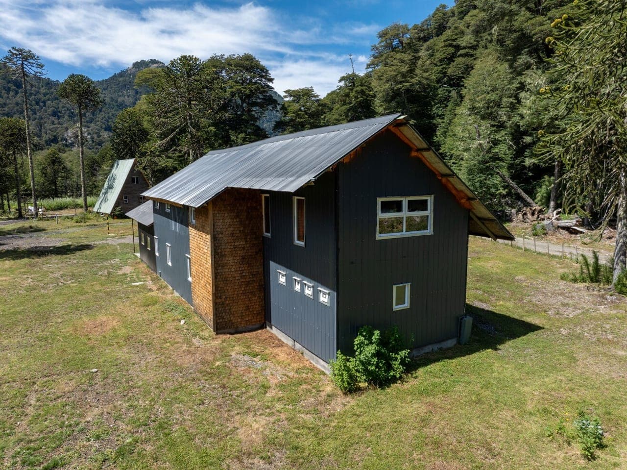 Exterior del refugio, revestido en tejuela y metal, con el cerro detrás